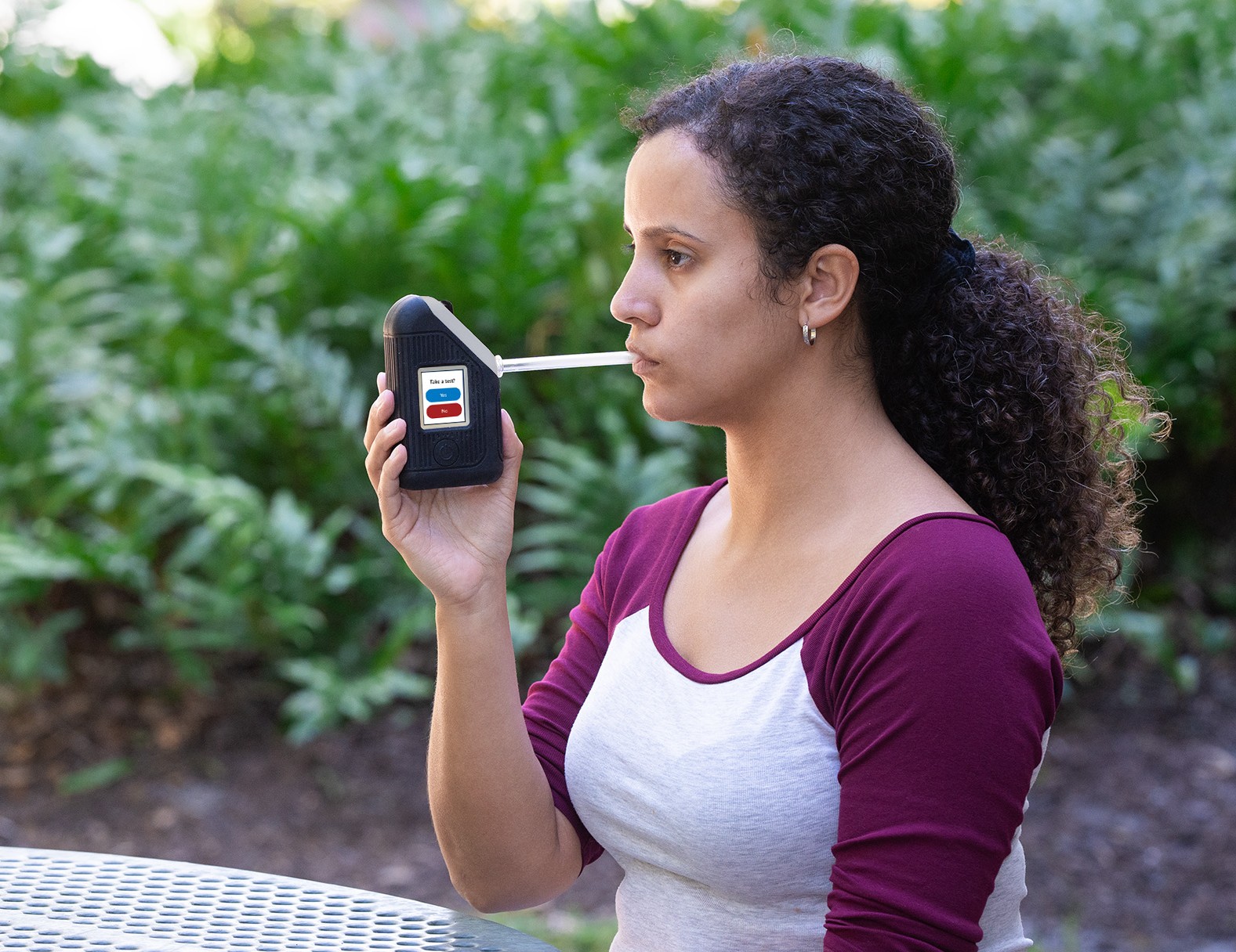 Woman using BI SoberTech alcohol monitoring device blows into straw to submit breath alcohol test.