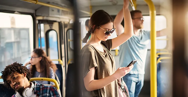 Young woman wearing sunglasses, engaged with her smartphone, promoting awareness for domestic violence survivor apps while commuting on a bus.