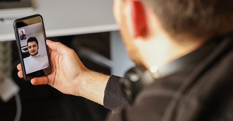 Two men engaged in a professional video call. One appears to be a supervision officer at a desk, while the other participant is shown in casual clothing in what appears to be a home setting. Both are looking at their screens with focused expressions during their remote check-in meeting.