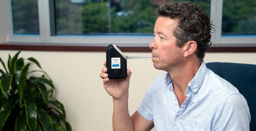 Alcohol testing technology in action: Man conducting a breath alcohol detection test at home using the compact BI SoberTech device