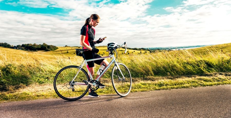 A woman in bike racing gear stopped in a field, looking at her phone and using a personal safety app.