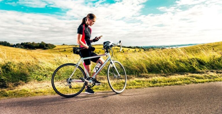 A woman in bike racing gear stopped in a field, looking at her phone and using a personal safety app.